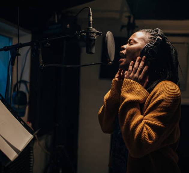 One woman, beautiful black female vocalist wearing headphones and singing into microphone in recording studio.